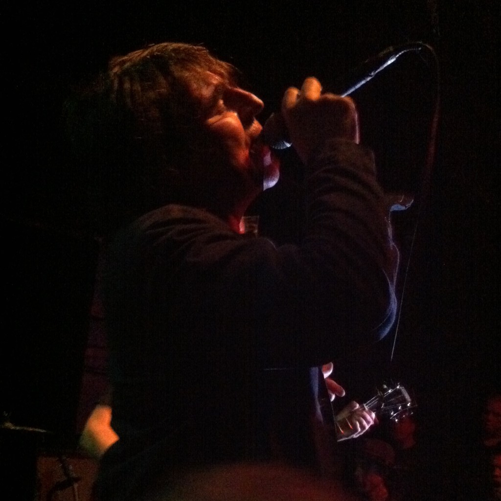 A man singing in profile, lit from above.